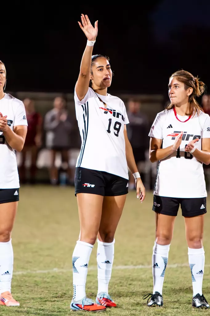 Sara Irurozki dressed in her soccer uniform in the field next to other players, waving at the crowd.